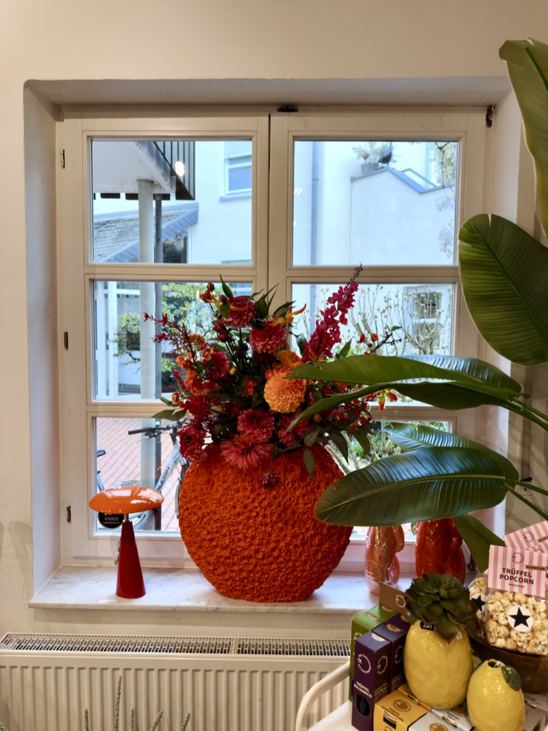 Orangefarbene Strukturvase mit herbstlichem Blumenarrangement am Fenster im Glüxstern